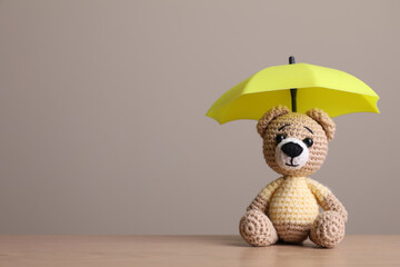 Small umbrella and toy bear on wooden table. Space for text