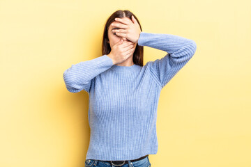 hispanic pretty woman covering face with both hands saying no to the camera! refusing pictures or...