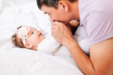Obraz na płótnie Canvas a newborn girl is lying with her young father in a snow-white bed. dad kisses the hands of his newborn daughter. the concept of the family