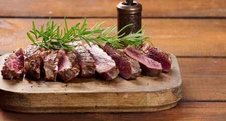fried piece of beef ribeye, cut into pieces on a brown wooden board, rare doneness