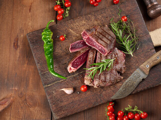 roasted piece of beef ribeye cut into pieces on a vintage brown chopping board, rare doneness. Delicious steak, top view