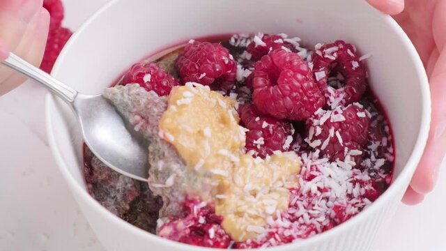 Eating chia pudding with raspberries, peanut butter and coconut with a spoon. Healthy vegan food concept.