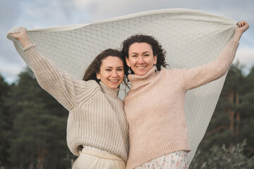 The two happiest women enjoy life and look into the distance. Girls in light sweaters with a large knitting. Gentle and warm wind blows on the girls