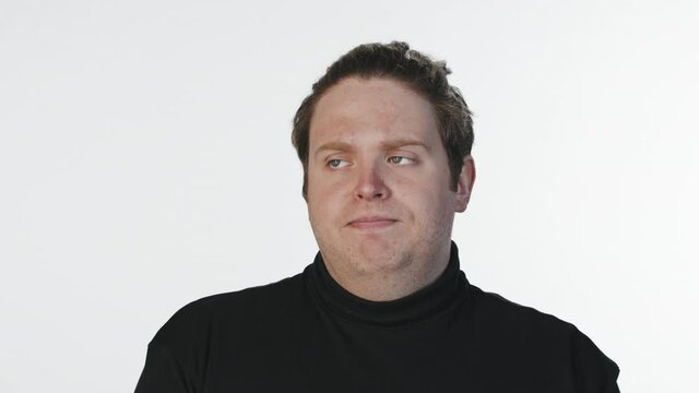 Medium close-up portrait with slowmo of bored or impatient man with poker face looking at camera exhaling deeply, standing at white background