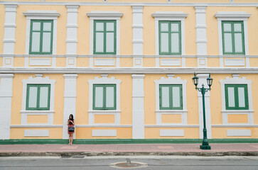 Obraz premium A girl stand alone colorful yellow Palladian architecture from European style at building Thai Ministry of Defense which is tourist center and old town in Thailand