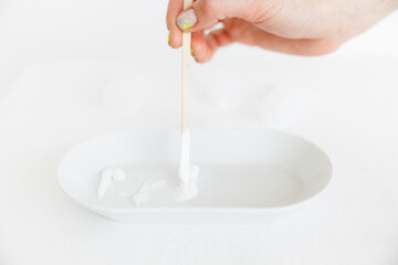 a wooden stick is placed in an oval saucer with a cosmetic cream. there are several cream textures in a white saucer on a white background. Cosmetology and care.