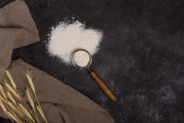 Flour in a plate with a flour scoop. The texture of the black background. Ears of wheat