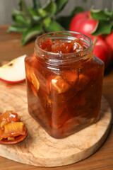 Tasty apple jam in glass jar on wooden table, closeup
