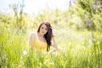 Naklejka na ściany i meble Young woman in yellow top sitting in grass in summer