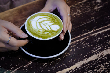 Woman hand holding cup of green tea matcha latte foam art is the most popular drink for modern...