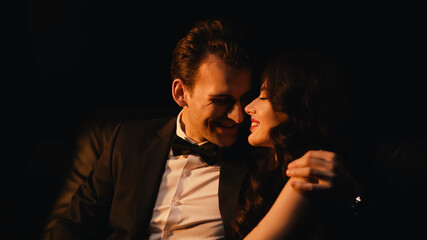 Obraz premium Smiling man in suit hugging and flirting with cheerful girlfriend isolated on black