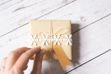 Woman's hand opening a Christmas present. Gift giving. Natural winter theme decoration, brown paper, twine, snowflake ribbon, name tag. Merry Christmas. Empty space for text. Copy space.