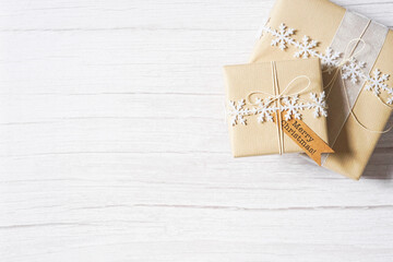 Christmas presents on white wooden background. Natural winter theme decoration, brown paper, twine, snowflake ribbon, tag. Sustainable gift wrapping. Merry Christmas. Empty space for text. Copy space.