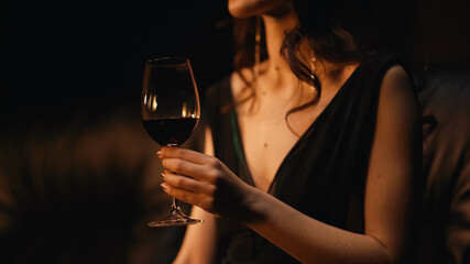 cropped view of elegant young woman holding glass of wine and sitting on sofa on black