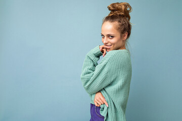 Young beautiful cute curly blonde woman with sexy expression, cheerful and happy face wearing trendy blue sweater isolated over blue background with copy space