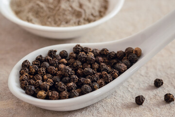 Black pepper corn on spoon and black pepper powder in bowl.