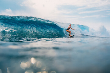 Surfer girl at surfboard on wave in tropical ocean. Sporty woman during surfing.