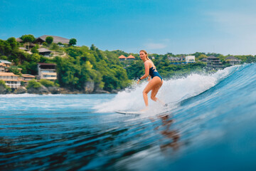 Surf girl at surfboard on blue wave in Bali, Impossibles beach. Sporty woman during surfing.