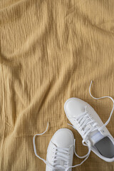 Fototapeta na wymiar Fashion blog or magazine concept. White female sneakers on yellow crumpled muslin cloth background. Flat lay, top view minimal background
