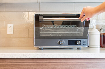 Hand pulling down a digital countertop oven door