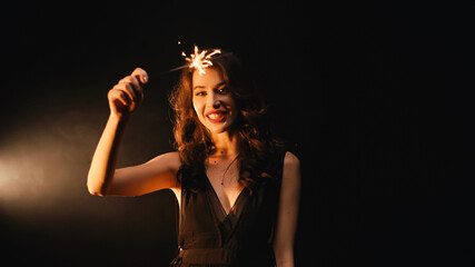 Positive young woman with sparkler smiling on black background