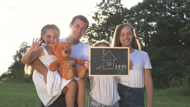 Happy family greets with smile, looks into camera.People welcome to camera by waving hand.family holds sign, looks into camera.Happy children with mom, dad are smiling, waving.Family at home outdoors.