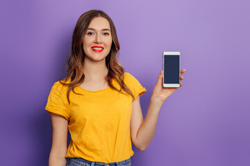 Young caucasian student girl shows a black phone screen isolated on a lilac background. Mockup