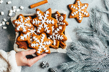 top view of Christmas glazed gingerbread cookies in a box in a female hand on a gray background