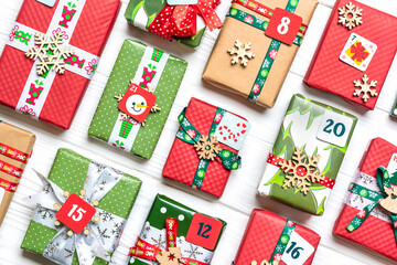 Fototapeta na wymiar Handmade wrapped red, green gift boxes decorated with ribbons, snowflakes and numbers, Christmas decorations and decor on white table Xmas advent calendar concept Top view Flat lay Holiday card