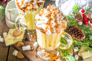 Homemade Salted Caramel Eggnog or White Hot Chocolate drink, with caramel sauce, whipped cream and marshmallow, on wooden background with Christmas winter decorations copy space