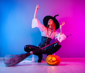 slender girl in a witch costume for Halloween with a broom and a pumpkin