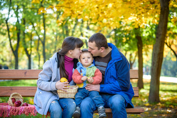 Naklejka na ściany i meble happy family enjoying autumn picnic. Father mother and son sit on bench with apples basket. Happy family leisure together concept