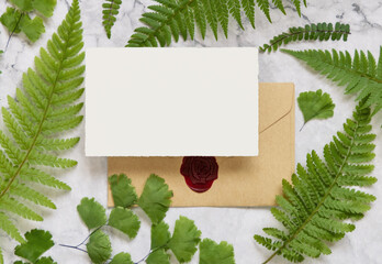 Blank paper card and envelope with fern leaves on marble table