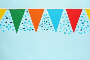 Bunting with colorful triangular flags and confetti on light blue background, flat lay. Space for text