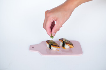 Japanese Sushi - Two Unagi Nigiri Sushi served on light pink board. Eel Sushi. Close-up view of process of preparing sushi. isolated on white