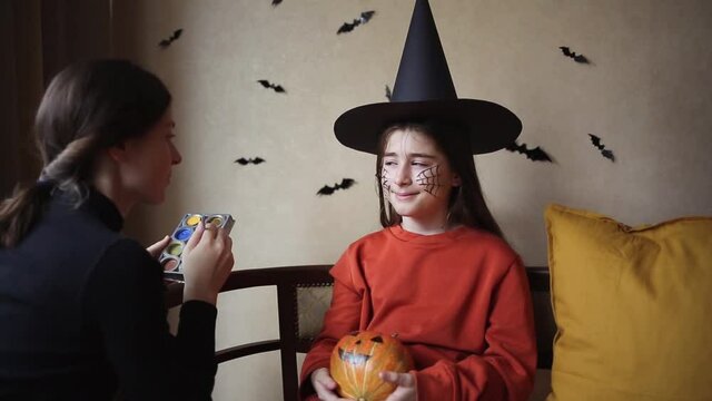 face paints for halloween. woman draws web for child with brush. mom and daughter are preparing for holiday at home.