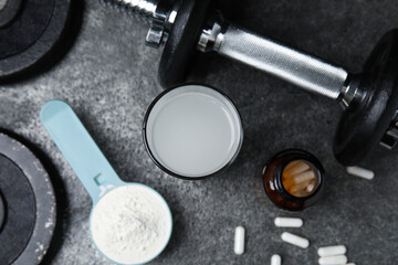 Amino acid shake, powder, pills and dumbbell on grey table, flat lay