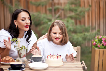 Happy adorable girl with mom celebrate with birthday cake in cafe terrace. 10 year old celebrate birthday.