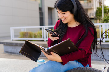 Fototapeta premium Young latin woman taking a picture to her notes of notebook outdoors