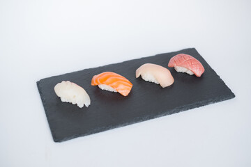 Four sushi nigiri served on the black slate on white background. Japanese traditional food. Up side view. High quality photo