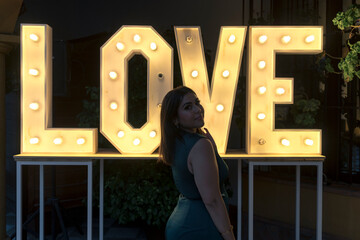 Chica guapa en vestido frente a un mural de luces con la palabra love con actitud 