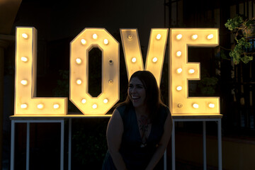 Chica guapa en vestido frente a un mural de luces con la palabra love con actitud 