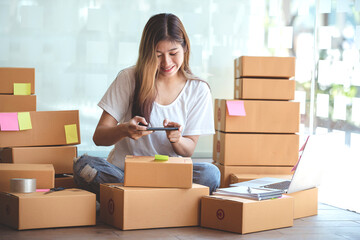 Young woman taking pictures during packaging with a mobile phone or smartphone digital camera to prepare the product box pack selling ideas online