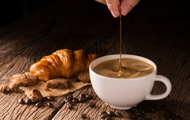 A cup of coffee mixed with milk or cream is placed on a dark wooden floor.