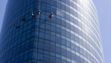 Five window washers hanging with ropes outside blue glass modern building. Risky job, dangerous...