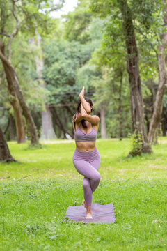 young woman in purple sportswear, doing yoga outdoors 