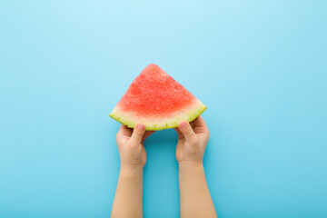 Baby hands holding red slice of watermelon on light blue table background. Pastel color. Closeup....