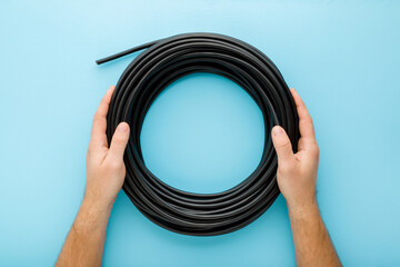 Young adult man hands holding black rolled cable on light blue table background. Pastel color....