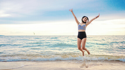 Fototapeta na wymiar Happy asian young woman in casual style fashion jumping at sand beach. Relaxing, fun, and enjoy holiday at tropical paradise beach with blue sky and white clouds. Girl in summer vacation.