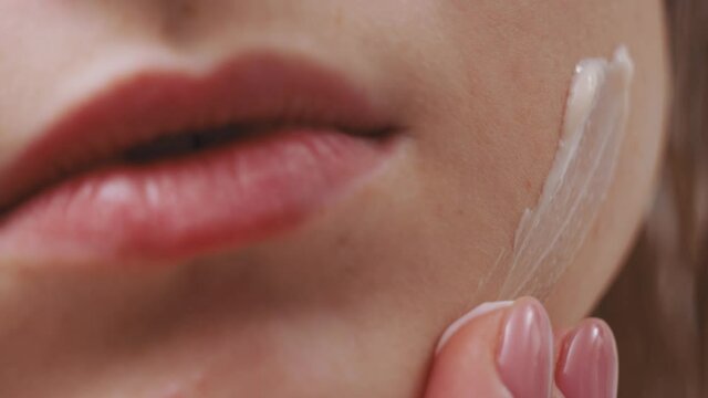 Macro closeup of young female face with beautiful white clear skin. Young adult girl applying facial creme for healthcare beuaty treatment.